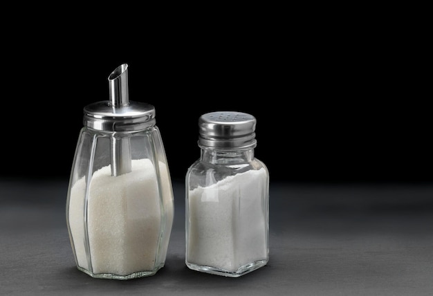 Sugar dispenser and and glass Salt shaker on slate black stone background