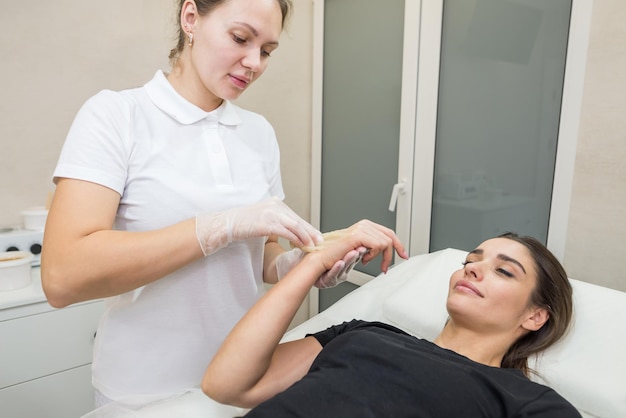 Sugar paste hair removal procedure shugaring Cosmetologist applies sugar paste to the hand of a young woman