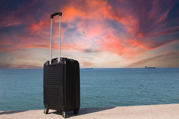 A suitcase is standing on a beach with a sunset in the background Travel and holiday consept