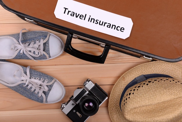 Suitcase and tourist stuff with inscription travel insurance on wooden background top view