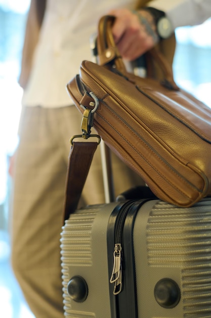 Suitcase with baggage and brown leather handbag held by young male traveler