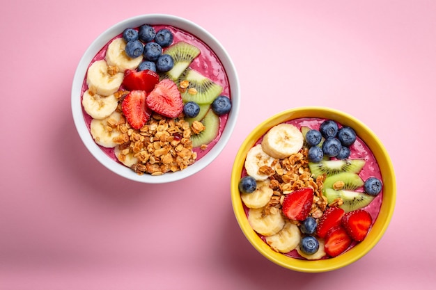 Summer acai smoothie bowl with strawberries, banana, blueberries, kiwi fruit and granola on pastel pink background. Breakfast bowl with fruit and cereal, close-up, top view, healthy food