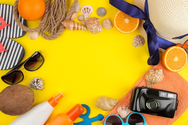 Summer accessories with sun glasses, a hat, shells, flip flops, a camera on a bright yellow background. top view.