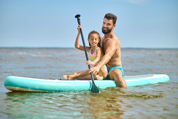 Summer activity. Young man in blue shorts kayaking with his daughter