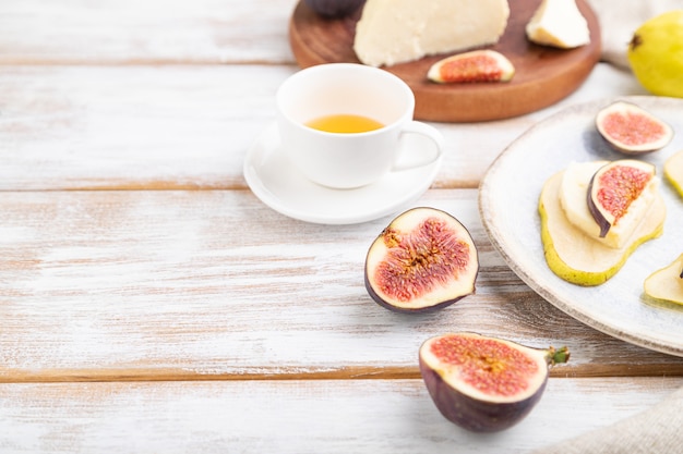 Summer appetizer with pear, cottage cheese, figs and honey on a white wooden background and linen textile. Side view, close up, selective focus.