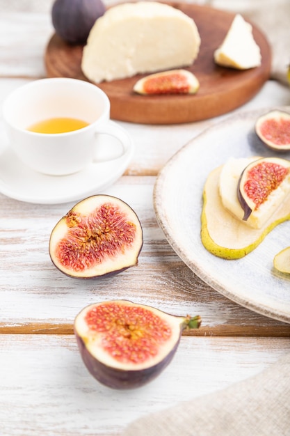 Summer appetizer with pear, cottage cheese, figs and honey on a white wooden background and linen textile. Side view, close up, selective focus.