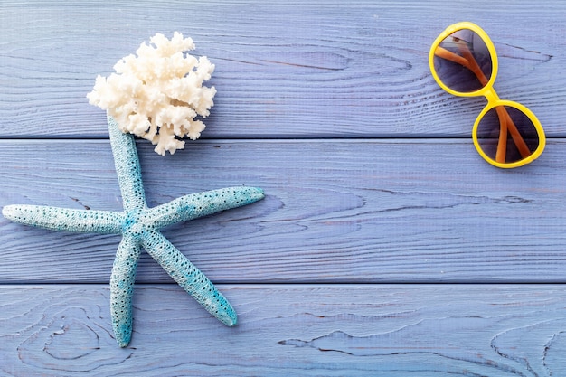 Summer backgroun starfish, coral, seashell, sunglasses on blue wooden background