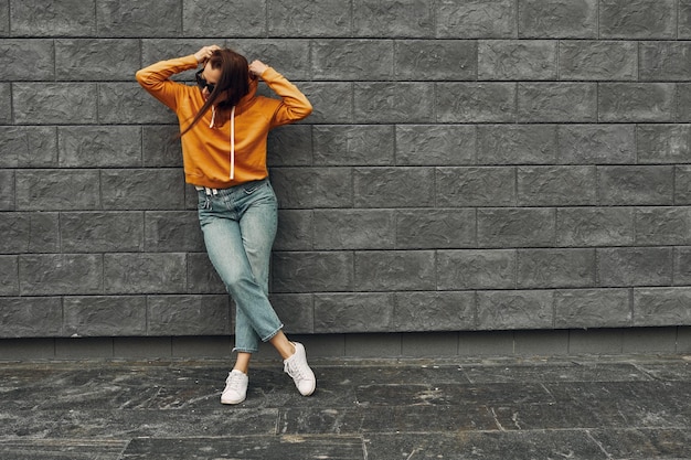 Summer background. Beautiful girl in an orange hoodie against a gray wall.