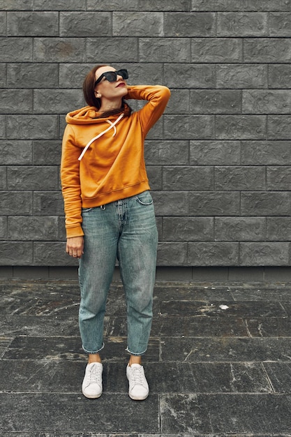 Summer background. Beautiful girl in an orange hoodie against gray wall.