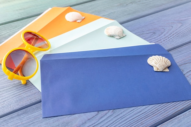 Summer background colorful envelopes, sunglasses, seashells on a blue wooden background