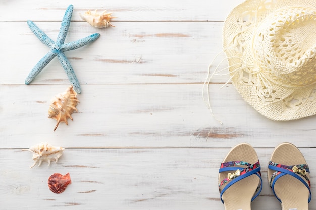 Summer background concept female sandals, starfish, seashells, straw hat on light wooden surface