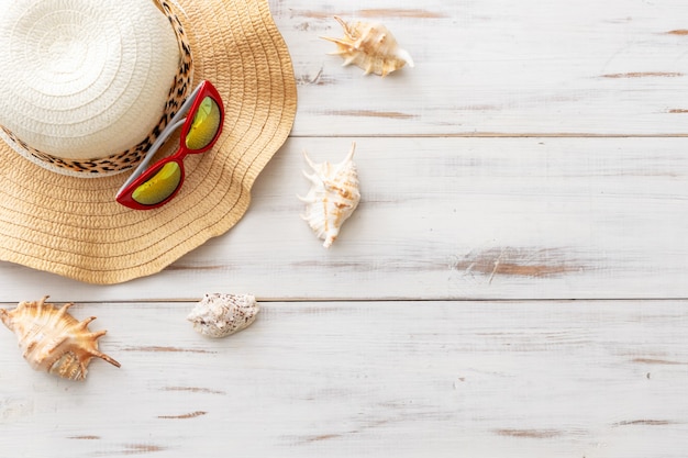 summer background concept straw hat, seashells, sunglasses on light wooden surface