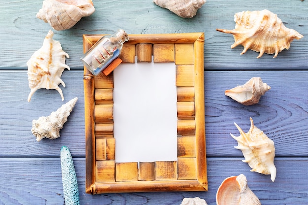 Summer background photo frame, seashells, coral, ship in a bottle on a blue wooden background