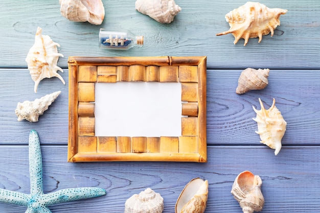 Summer background photo frame, seashells, coral, ship in a bottle on a blue wooden background