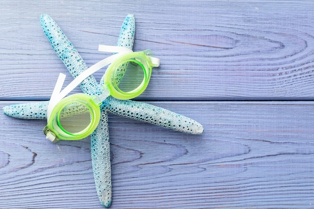 Summer background starfish, swimming goggles on blue wooden background