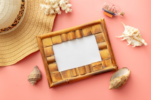 Summer background of straw hat, photo frame, shells, coral on pink background