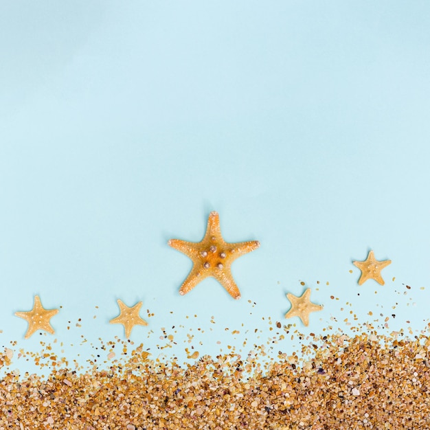 Summer background with yellow seastar and sand on pastel blue Concept of travel and vacation