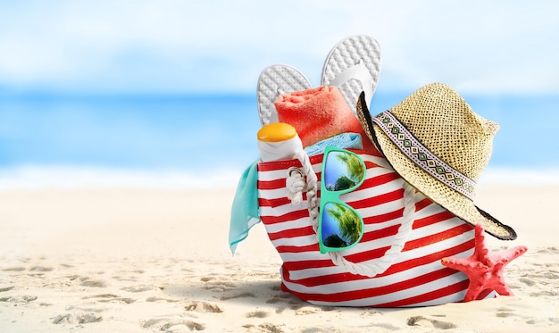 Summer beach bag and accessories on sandy beach and sea