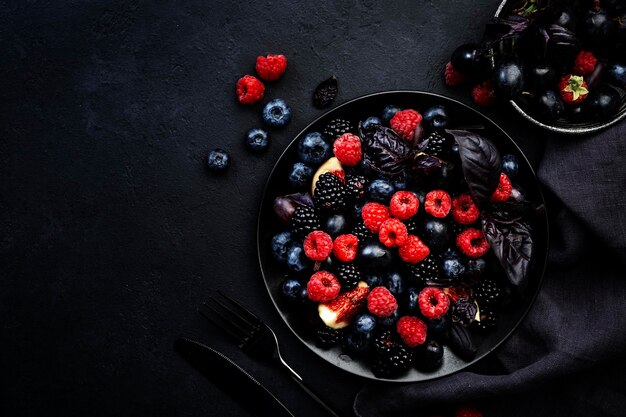 Summer blue and black berries fruit vegan salad blueberries blackberries grapes figs and purple basil with honey dressing on dark background top view