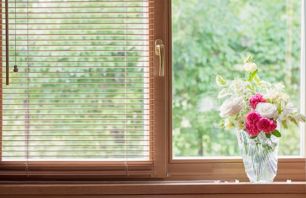 Summer bouquet in glass vase  on windowsill in wooden house