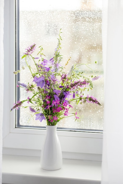 Summer bouquet on white windowsill witrh rain drops