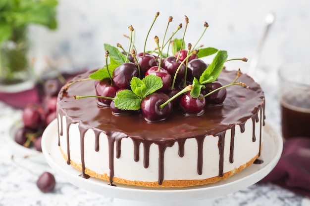 Summer cake with chocolate topping decorated fresh cherries on a white cake stand