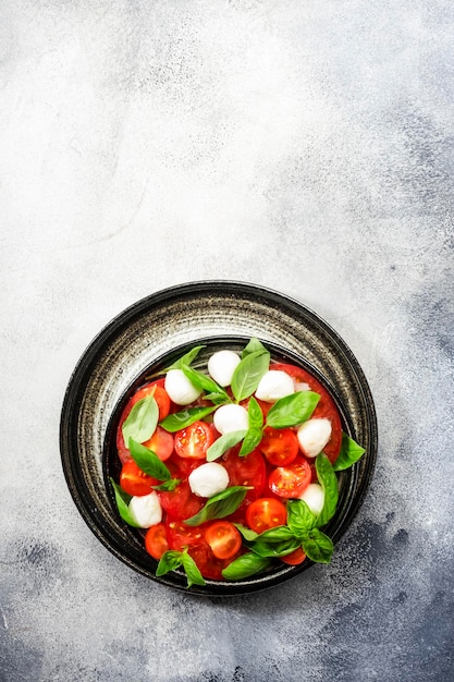 Summer caprese salad with red tomatoes and white mozzarella cheese with fresh green basil leaves Gray table Top view