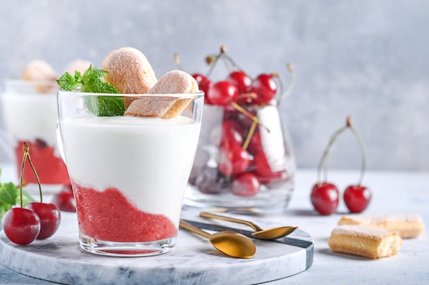 Summer cherry puff pastry with savoiardi cookies and cream cheese in glass on light grey background. Traditional tiramisu cake with fresh berries. Selective focus.