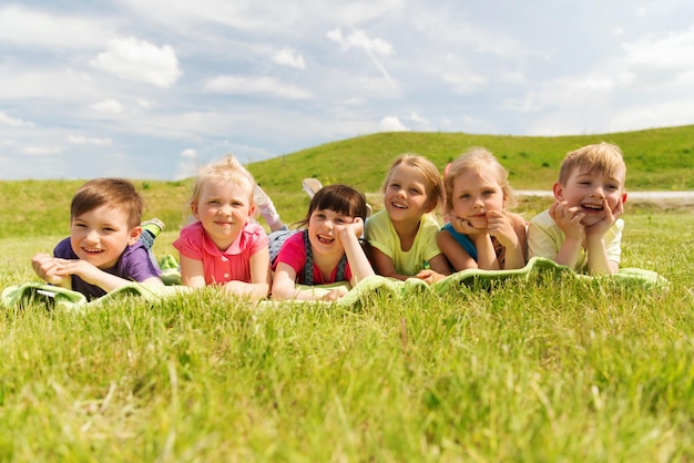 summer, childhood, leisure and people concept - group of happy kids lying on blanket or cover outdoors