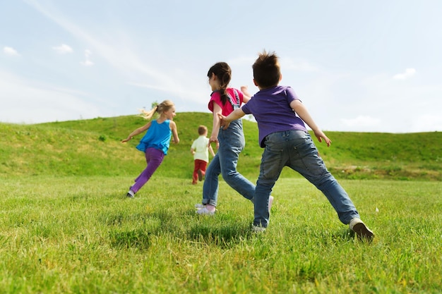 summer, childhood, leisure and people concept - group of happy kids playing tag game and running on green field outdoors