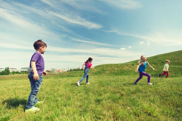 summer, childhood, leisure and people concept - group of happy kids playing tag game and running on green field outdoors