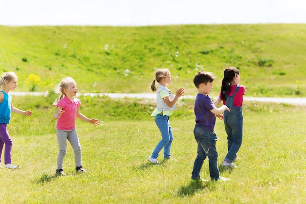 summer, childhood, leisure and people concept - group of little kind catching soap bubbles outdoors