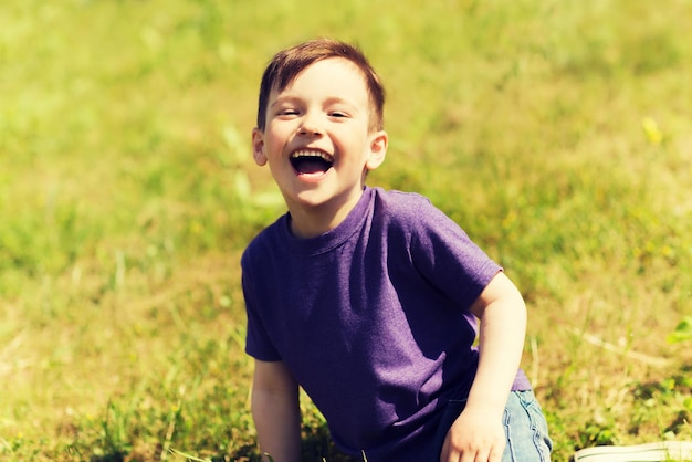 summer, childhood, leisure and people concept - happy little boy sitting on grass and laughing outdoors