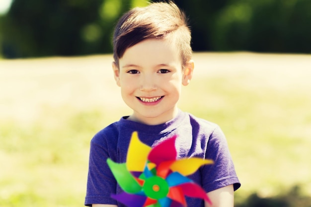 summer, childhood, leisure and people concept - happy little boy with colorful pinwheel toy outdoors