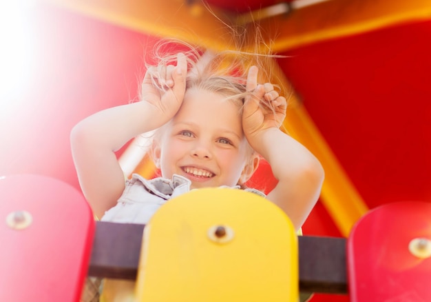 summer, childhood, leisure and people concept - happy little girl on playground climbing frame