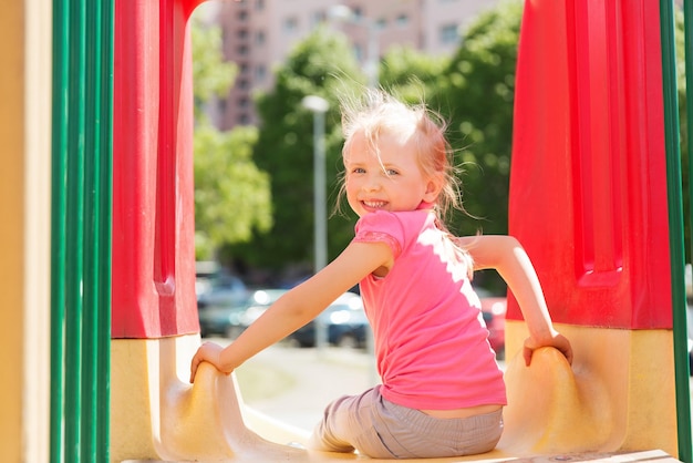 summer, childhood, leisure and people concept - happy little girl on slide at children playground