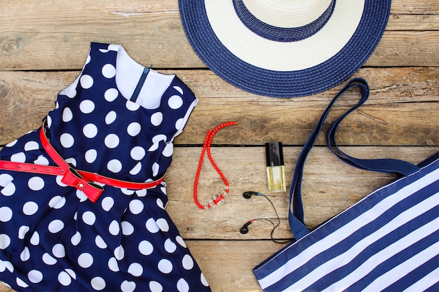 Summer clothing and accessories: dress, purse, hat, headphones, perfume, handbag and beads on old wooden background. 