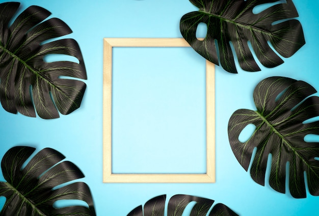 Summer composition with monstera leaves and frame Tropical leaves, empty photo frame on pastel blue background.