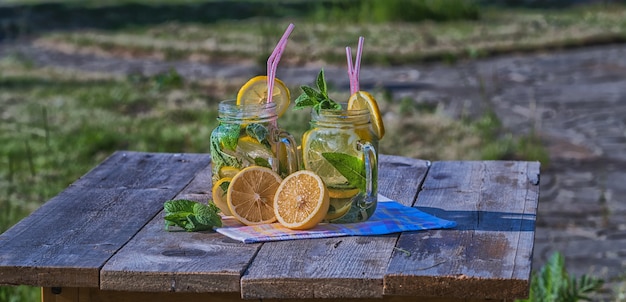 Summer concept. Homemade Lemonade with lemon, mint and ice in glasses, on wooden table, outdoor.