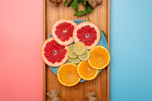 Photo summer concept sliced grapefruit, orange, lemon on wooden tray on pink and blue background