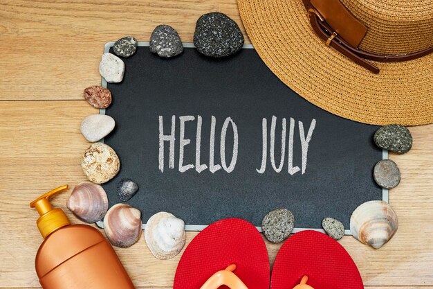 Photo summer concept sun cream and slipper with hello july text on chalkboard and stones seashell hat on