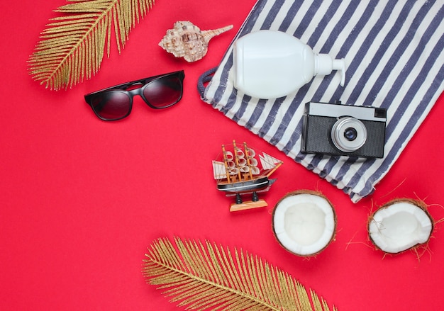 Summer creative background. Beach striped bag, accessories on red background. Top view.