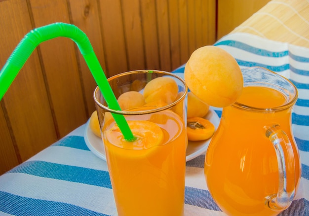 Summer drink apricot juice in a glass jug and in a glass glass Cup with straw and straw