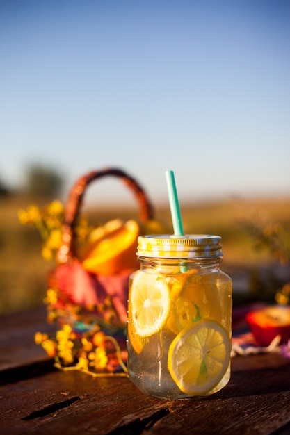 Summer drink in jar and basket with summer fruits in the sun, outdoor picnic or party concept