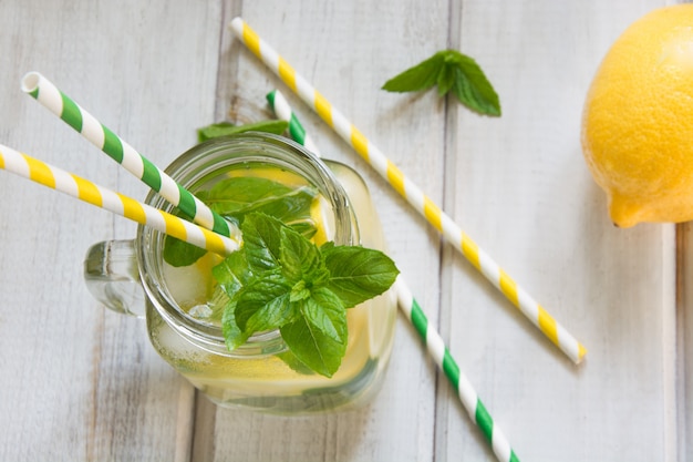 Summer drink, water detox with lemon, ice and mint in mason jar on a white wooden background.