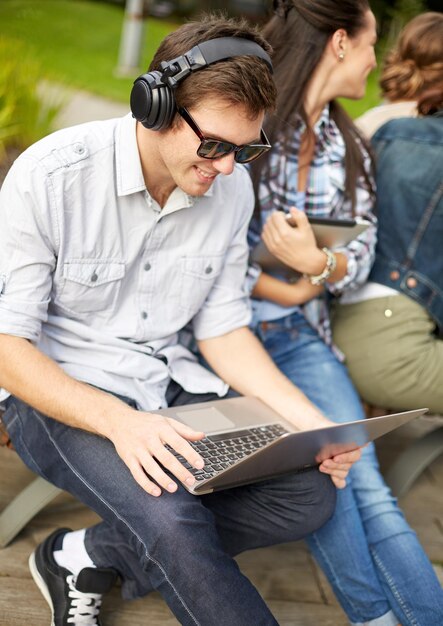 Photo summer, education, technology and people concept - group of students or teenagers with laptop computers sitting on bench outdoors