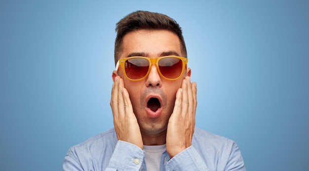 summer, emotions, style and people concept - face of scared or surprised middle aged latin man in shirt and sunglasses over blue background