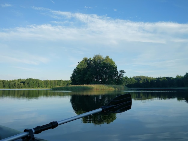 Summer evening landscape with lake surface and fragment of paddle of inflatable boat. Latvia, East Europe. Small island and calm water.