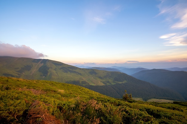 Summer evening mountain landscape with grassy hills and distant peaks at colorful sunset.