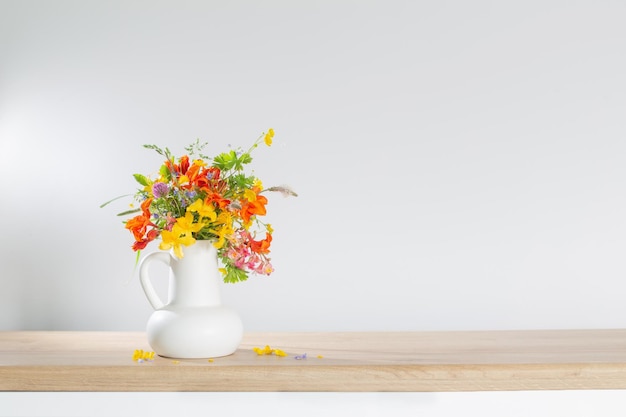 Summer flowers in white jug on wooden table